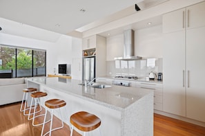 A modern kitchen with a central island, bar stools, stainless steel appliances, and a large window. - St Johns Wood Treehouse (Blairgowrie)