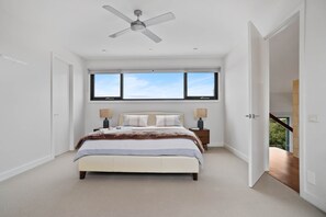 Une chambre à coucher avec un lit, deux tables de chevet, un ventilateur de plafond et une grande fenêtre.