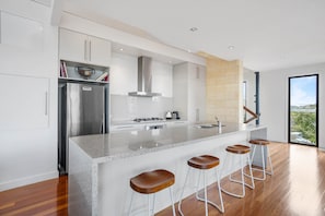A modern kitchen with a central island, stainless steel appliances, and a view to the outdoors. - St Johns Wood Treehouse (Blairgowrie)