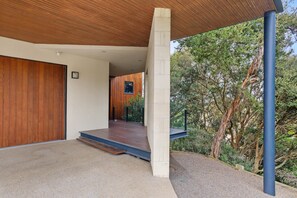 A modern building with a wooden facade, a concrete pillar, and a view of trees. - St Johns Wood Treehouse (Blairgowrie)
