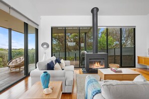 Ein modernes Wohnzimmer mit Kamin, einer Couch, einem Couchtisch und einem großen Fenster mit Blick ins Freie.
