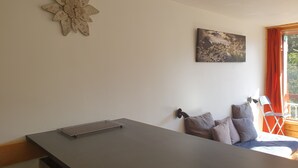 Une pièce comprenant un lit, un bureau, une horloge murale, un tableau et une fenêtre avec des rideaux.