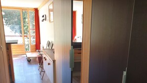 Un couloir avec un plancher en bois, un bureau avec une chaise et une fenêtre ornée de rideaux rouges.