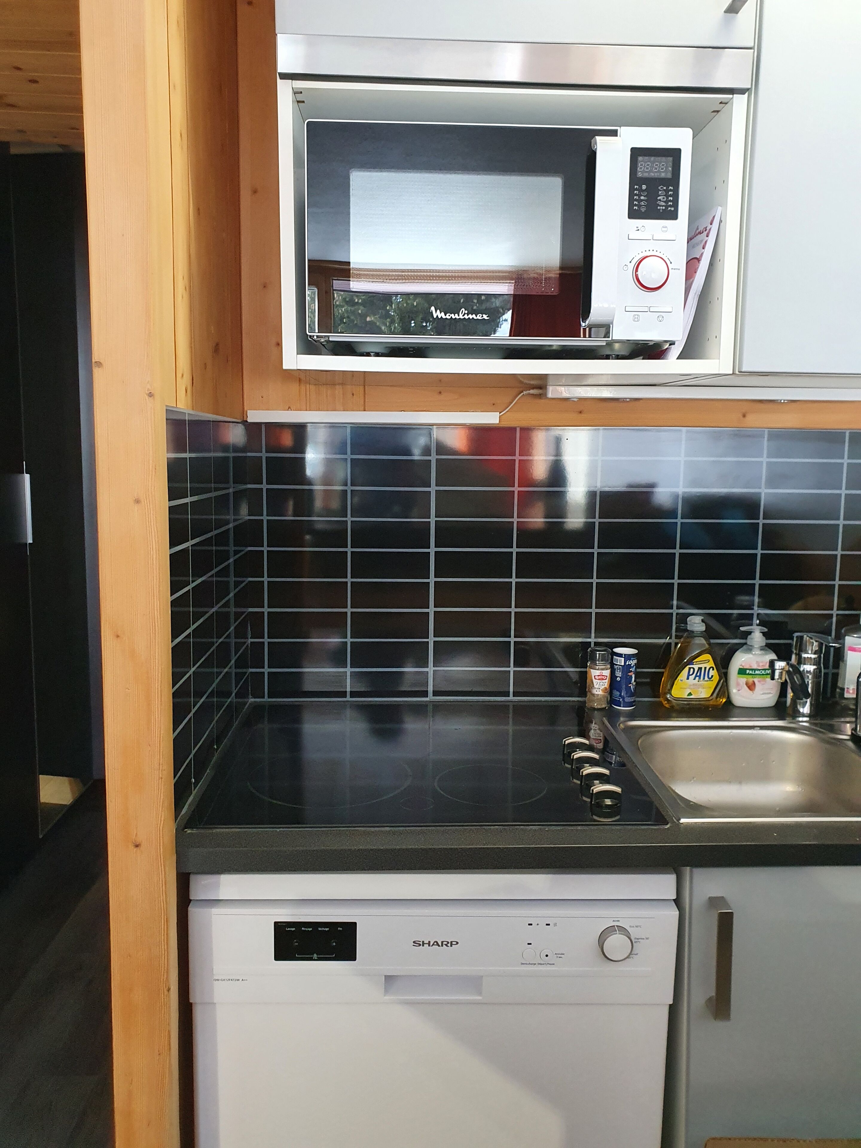 A compact kitchen with a microwave, dishwasher, and tiled backsplash.