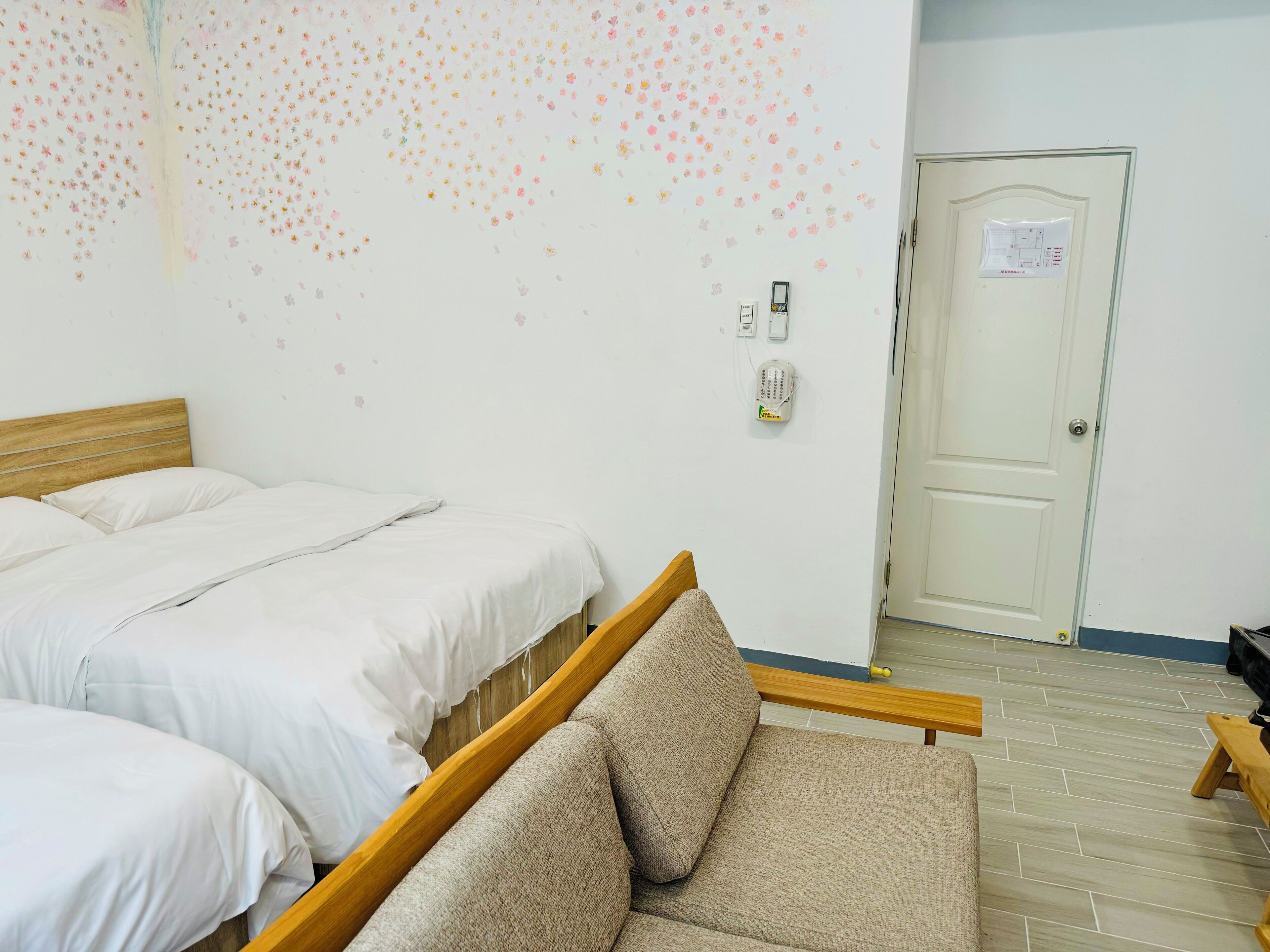 A hotel room with two beds, a sofa, a wall-mounted phone, and a door with a map.