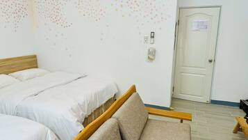 A hotel room with two beds, a sofa, a wall-mounted phone, and a door with a map.
