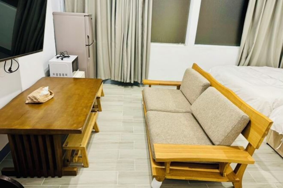 A compact room with a wooden dining table, a sofa, a bed, a television, and a microwave.