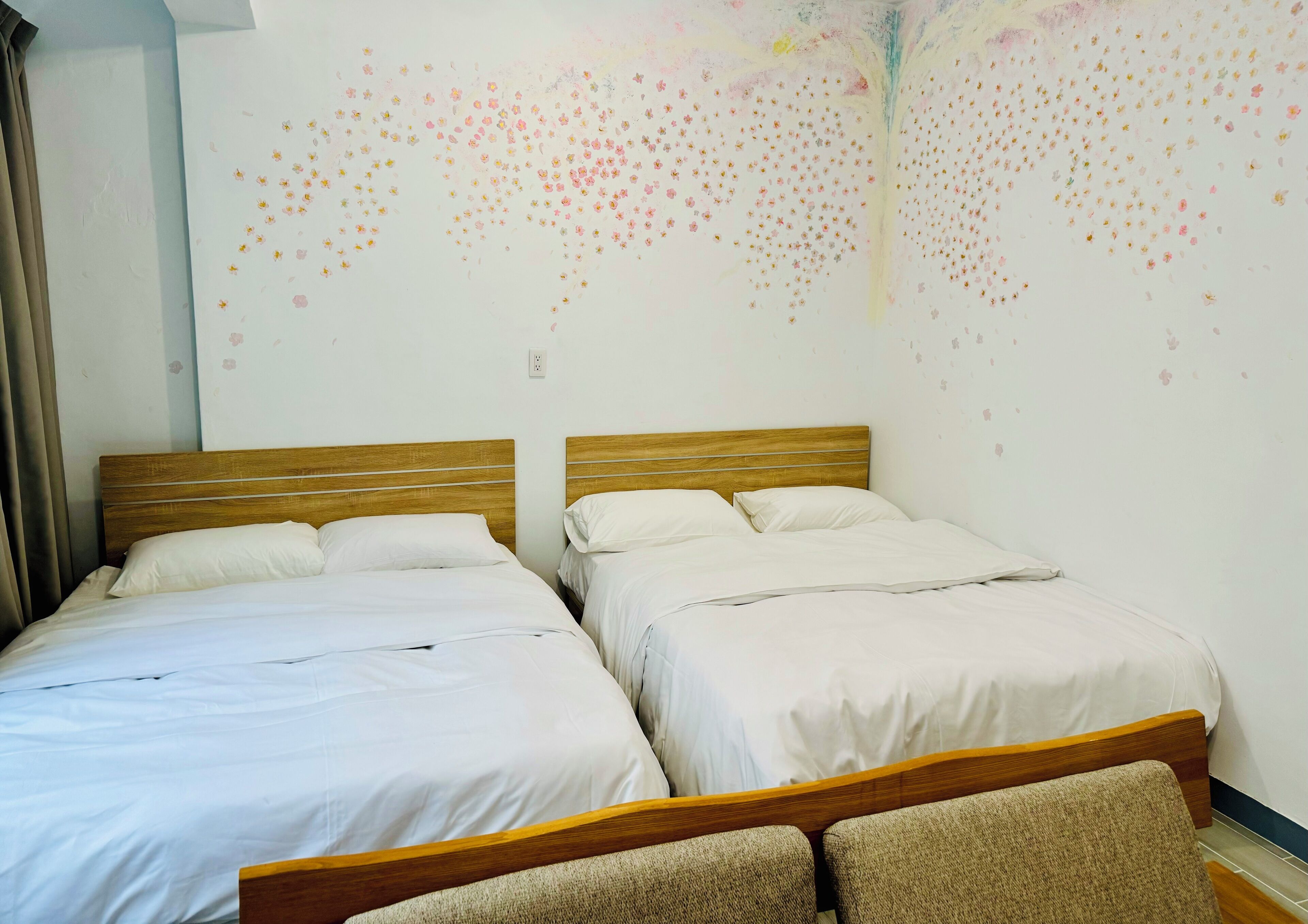 A room with two beds, wooden headboards, white bedding, and a wall with a floral pattern.