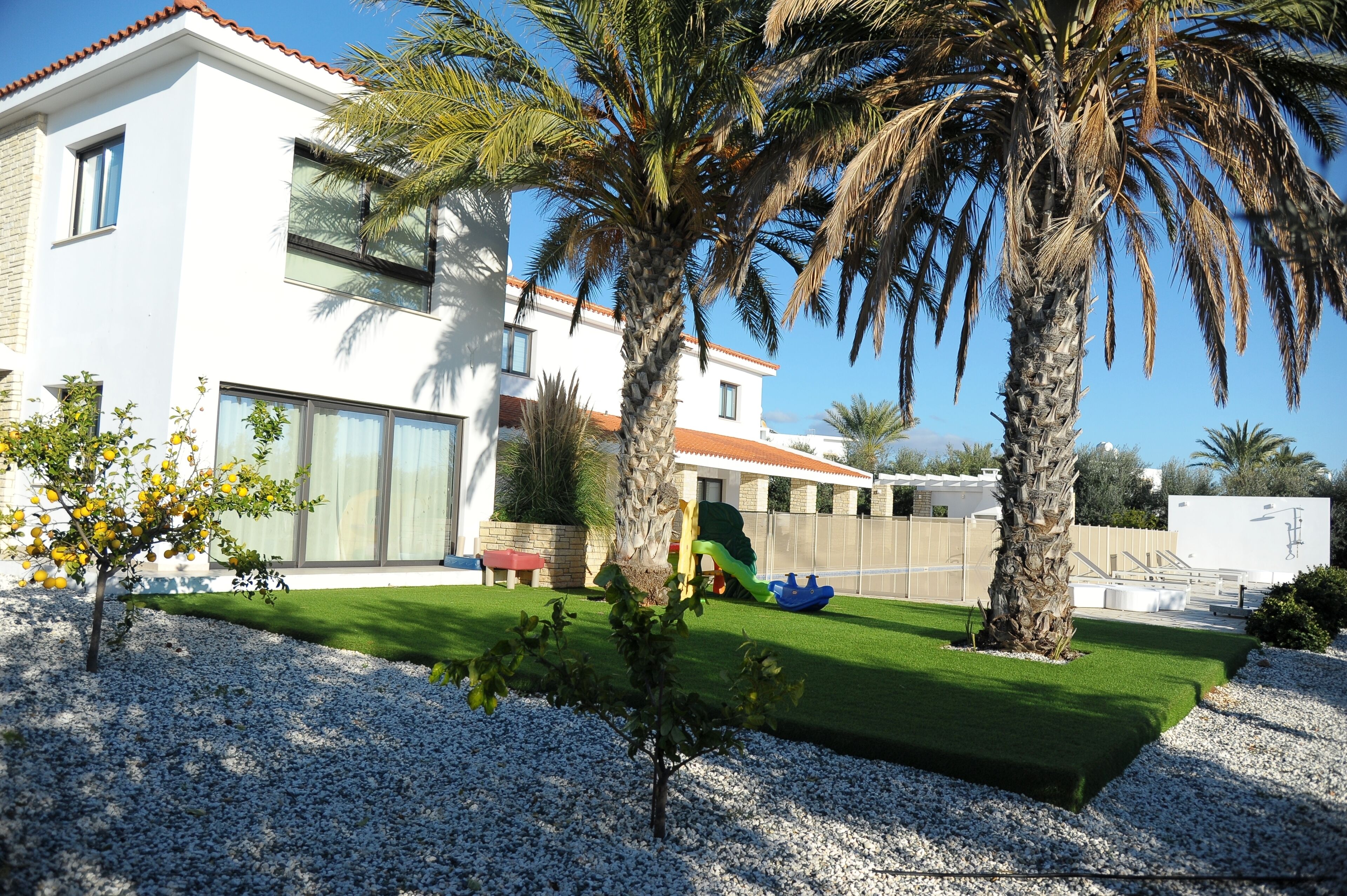A modern house with a white exterior, a green lawn, and a palm tree.