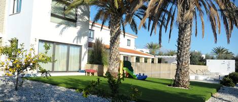 A modern house with a white exterior, a green lawn, and a palm tree.
