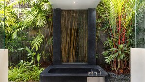 A modern spa area with a black jacuzzi, a waterfall feature, and lush tropical plants. - Villa Alice Dua by Villa Finder (Seminyak)