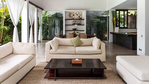 A modern living room with a beige sofa, a coffee table, and a dining area with a table and chairs. - Villa Alice Dua by Villa Finder (Seminyak)