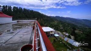 Una terraza en la azotea con techo rojo, un edificio blanco y vistas a un paisaje montañoso.