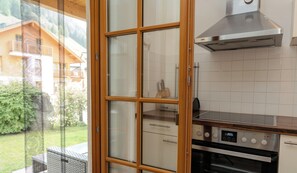 A kitchen with a stainless steel range hood, a built-in oven, and a window with a view of a house and greenery.