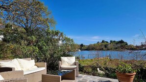 An outdoor seating area with wicker furniture and a view of a lake. - Cosy House in Eigionfa (Menai Bridge)