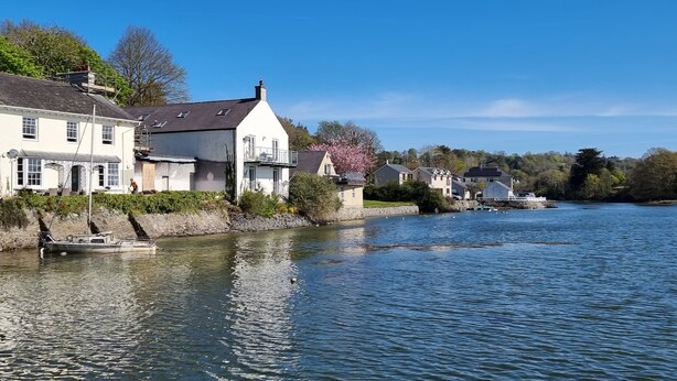 A riverside town with houses along the water, a boat docked near the shore, and a clear blue sky. - Cosy House in Eigionfa (Menai Bridge)