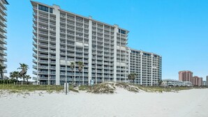 Un hotel moderno de gran altura con varios balcones, situado junto a una playa de arena.