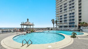 Un área de piscina en la azotea con dos piscinas, un pabellón y un rascacielos al fondo.
