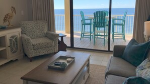Un salón con sofá, sillón y mesa de centro. Se ve el océano a través de amplios ventanales.