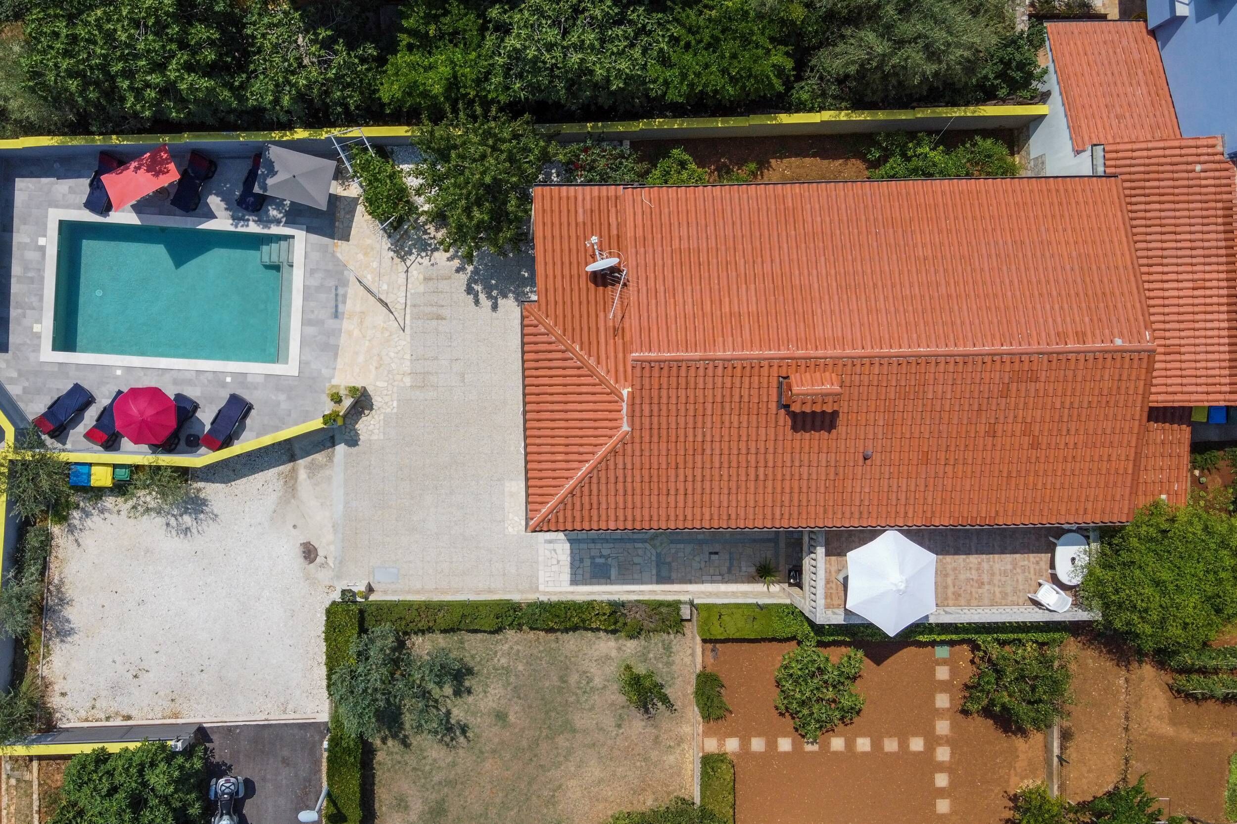 An aerial view of a property with a swimming pool, outdoor seating, and a red-tiled roof.