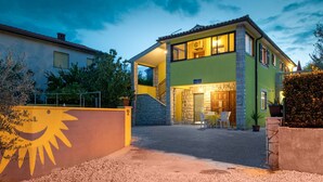 Une maison à deux étages avec une façade en pierre, un balcon et une entrée bien éclairée.
