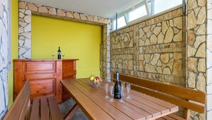 Une table en bois avec une bouteille et des verres, un panier de fruits et un mur en pierre.