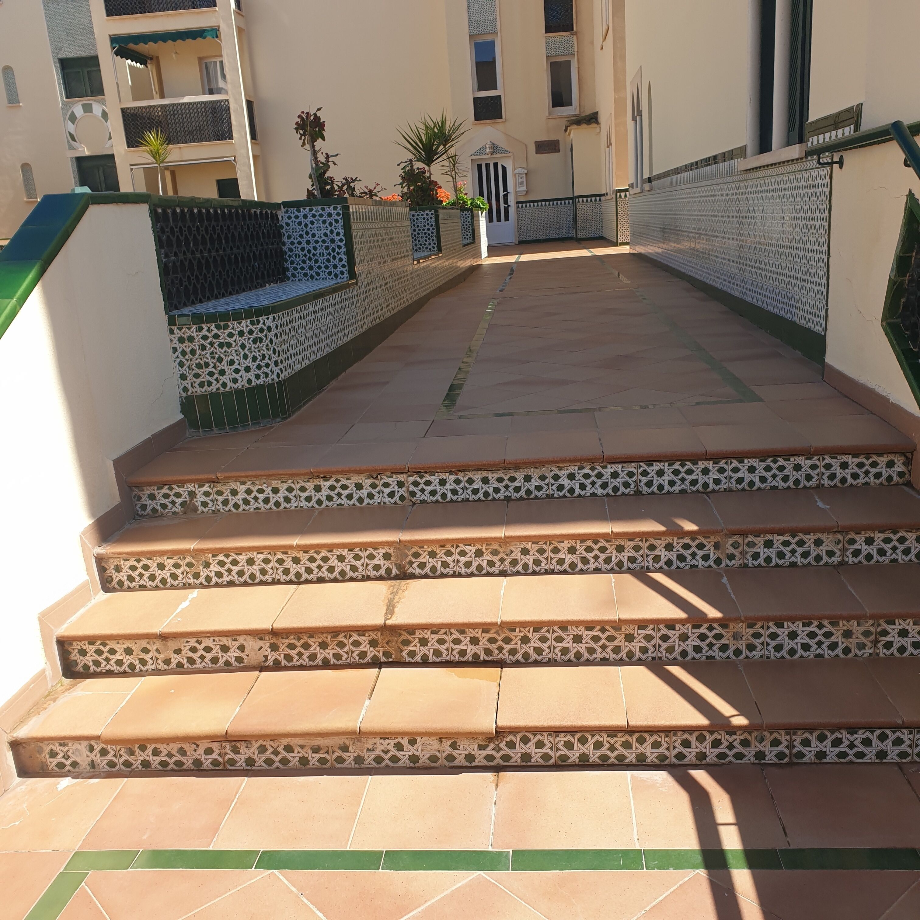 A set of outdoor stairs leading to a building entrance with patterned railings and a tiled floor.