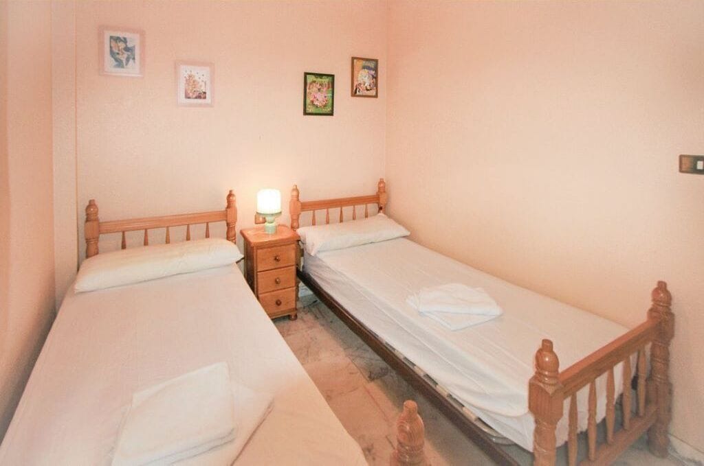 A bedroom with two single beds, a bedside table with a lamp, and three framed pictures on the wall.
