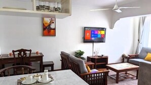 Ein Wohnzimmer mit Essbereich, einem an der Wand montierten Fernseher und einem Deckenventilator.