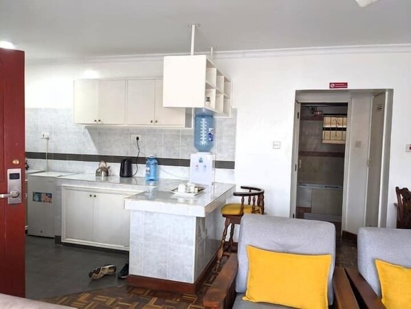Un espace de vie compact comprenant un coin cuisine, une petite table à manger et deux canapés avec des coussins jaunes.