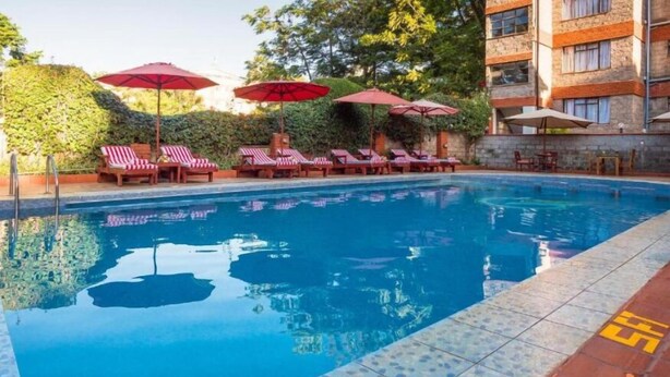 Ein Swimmingpool mit Liegestühlen und Sonnenschirmen, umgeben von Grünflächen und einem Gebäude.