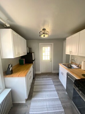 A compact kitchen with white cabinets, a wooden countertop, a built-in dishwasher, and a black stove. - Cute & Cozy 2 Bedroom House, In Heart of Town (Charlottesville)