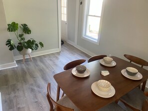 A dining area with a wooden table set for four, surrounded by chairs. A potted plant is visible in the corner. - Cute & Cozy 2 Bedroom House, In Heart of Town (Charlottesville)