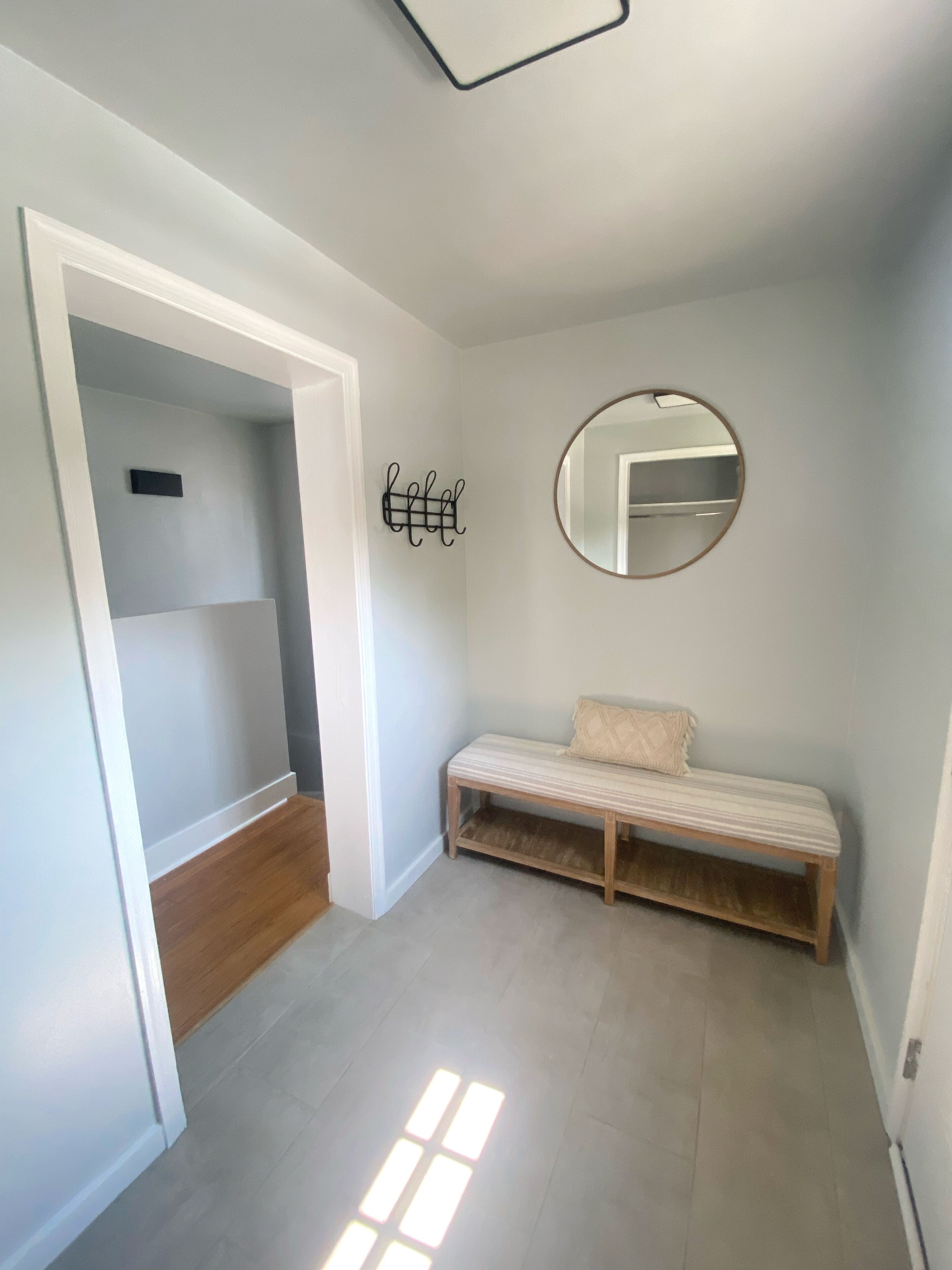 A room with a bench, a round mirror, and a wall-mounted rack.