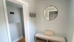 Una habitación con un banco, un espejo redondo y un perchero de pared.