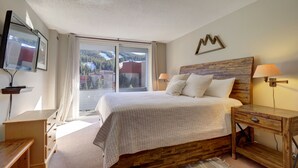 Ein Schlafzimmer mit einem großen Bett, einem Holzkopfstück, Nachttischen und Blick auf Berge durch das Fenster.