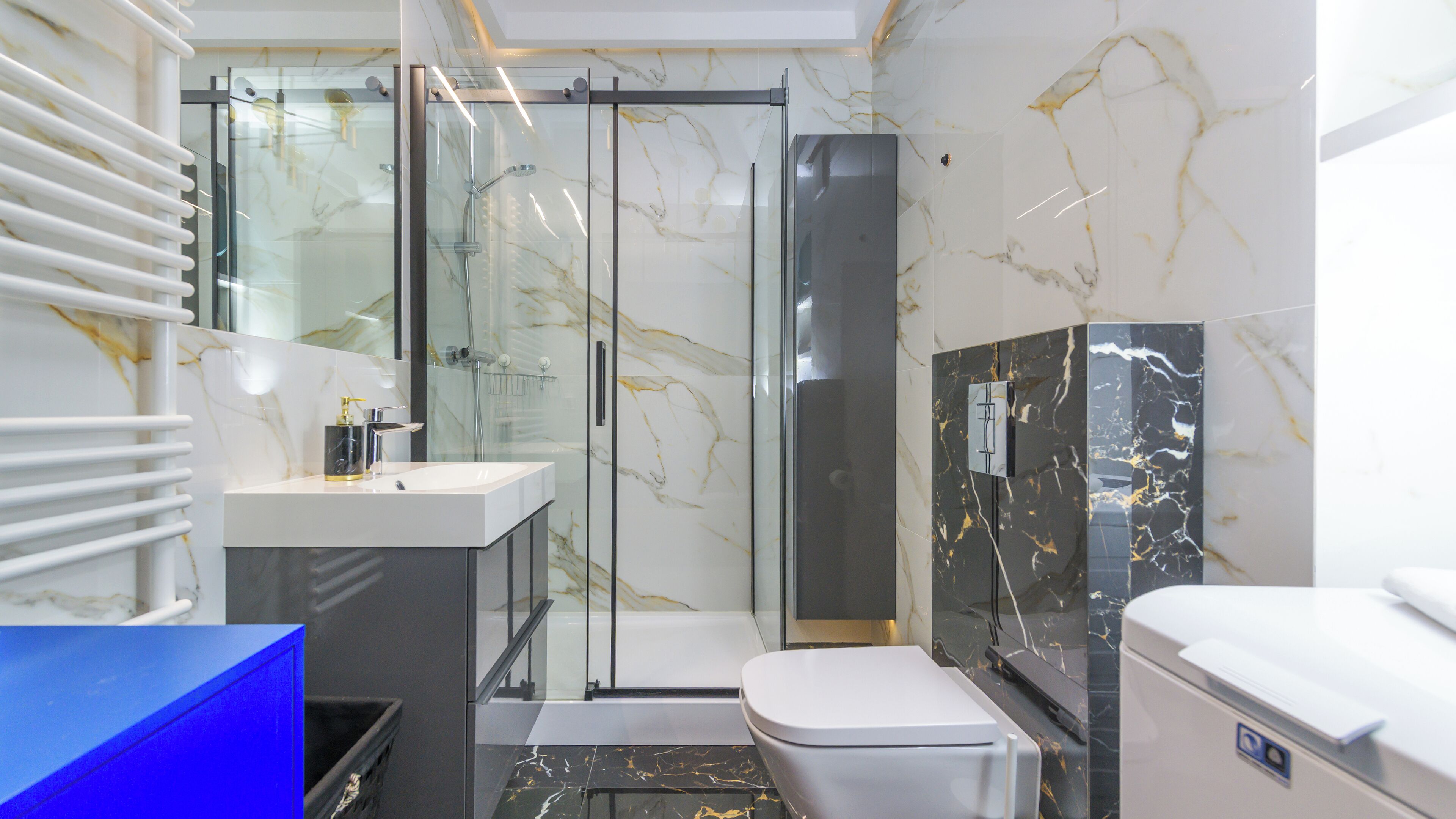 Een moderne badkamer met een glazen douchecabine, een wit toilet en een marmeren spatwand.