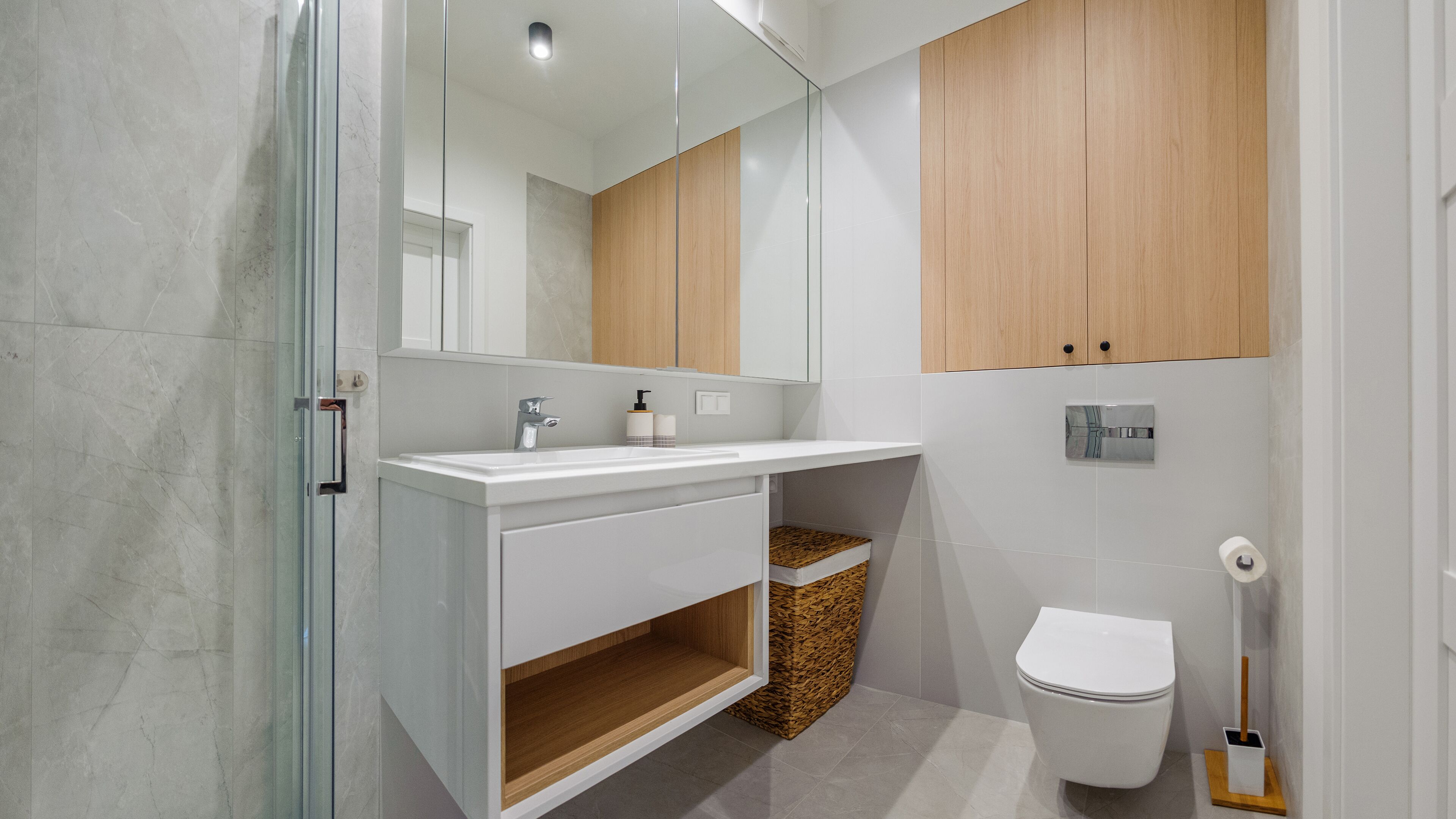 A modern bathroom with a glass shower enclosure, a white vanity with a mirror, a wooden cabinet, and a toilet.