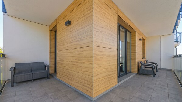 A modern outdoor area with a wooden partition, a grey wicker sofa, and a seating area with chairs.