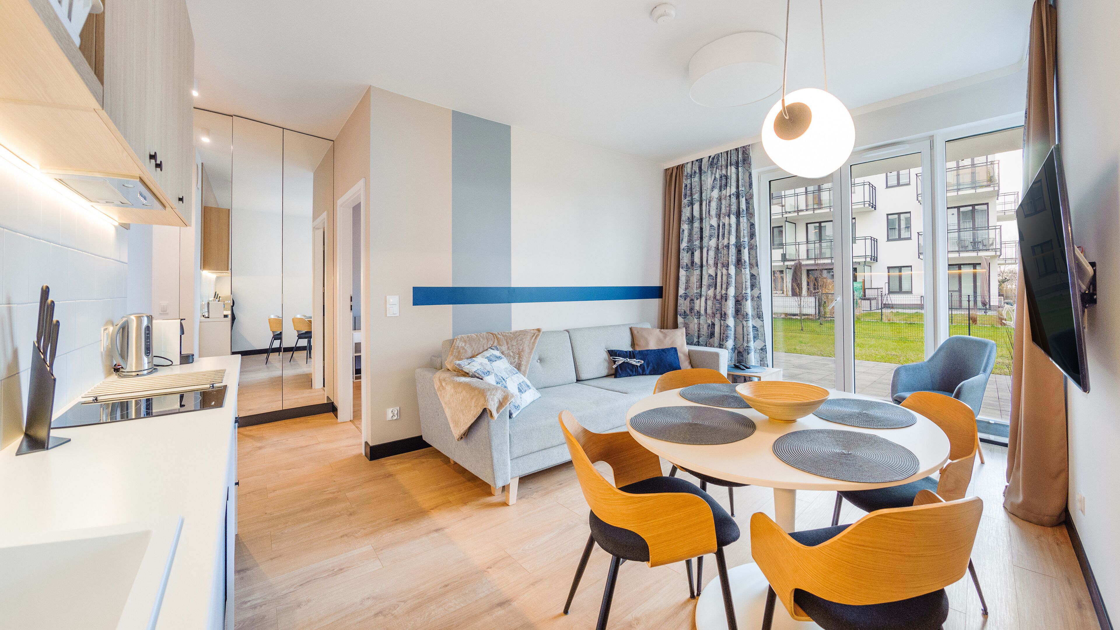 Un salon moderne avec un canapé, une table à manger et des chaises, ainsi qu’une grande fenêtre donnant sur des immeubles.
