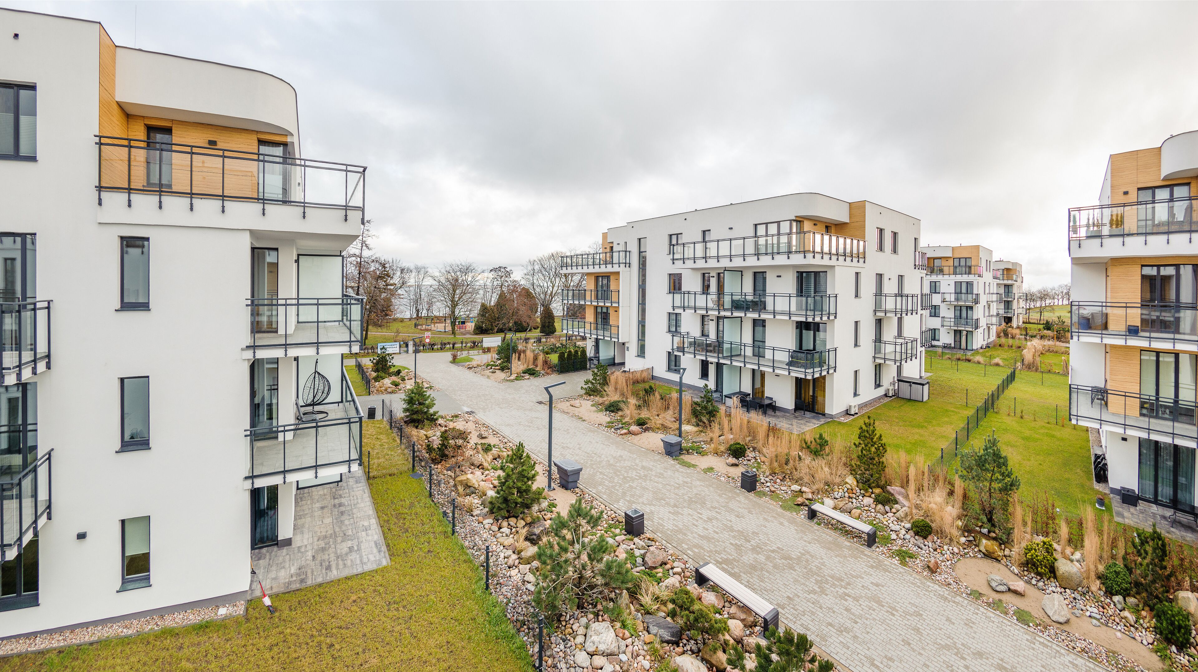 A modern residential complex with multiple balconies, a paved walkway, and landscaped areas.