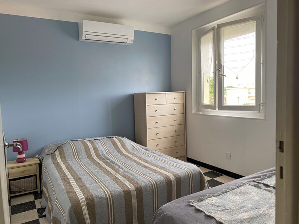 A bedroom with a bed, a dresser, a nightstand, and a window with a view. - Apartment 100 meters from the beach (Canet-Plage)