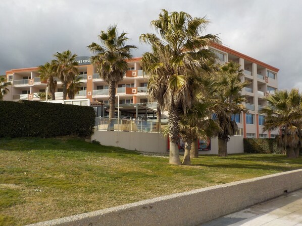 Un hotel de varios pisos con balcones, palmeras y un área verde al frente.