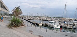 A marina with numerous boats docked, a pedestrian walkway, and a building with large windows. - Apartment 100 meters from the beach (Canet-Plage)