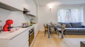 Une cuisine moderne avec un appareil électroménager rouge, un coin repas avec une table et des chaises, et un canapé gris dans un salon doté d’une fenêtre.
