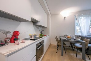 A modern kitchen with a red coffee maker, a dining table with chairs, and a window with curtains. - Res. San Marco 1 (Lugano)
