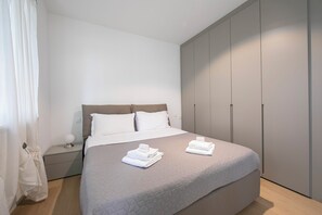 A modern bedroom with a large bed, grey wardrobe, and a bedside table with a lamp. - Res. San Marco 1 With Private Garden (Lugano)