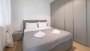 Une chambre moderne avec un grand lit, une armoire grise et une table de chevet avec une lampe.