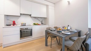 Une cuisine moderne avec des meubles blancs, un four encastré et un coin repas comprenant une table et des chaises en verre.