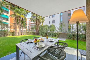 An outdoor dining area with a table set for four, surrounded by greenery and a view of buildings. - Res. San Marco 1 With Private Garden (Lugano)